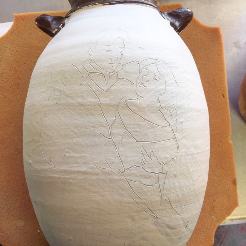 Unfired ceramic vase lying horizontal on a piece of foam. The image of two women is lightly indented into the surface.